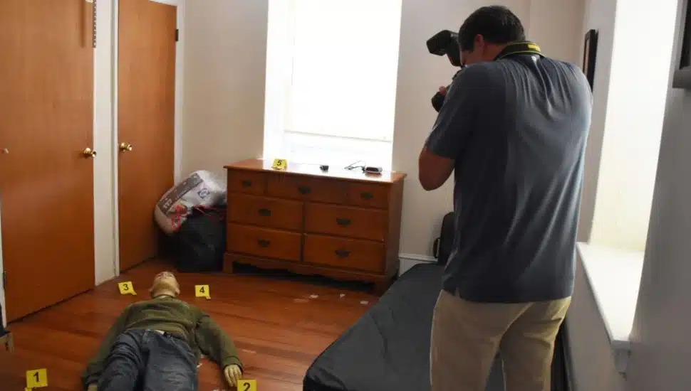 Man photographs mannequin in simulated crime scene.