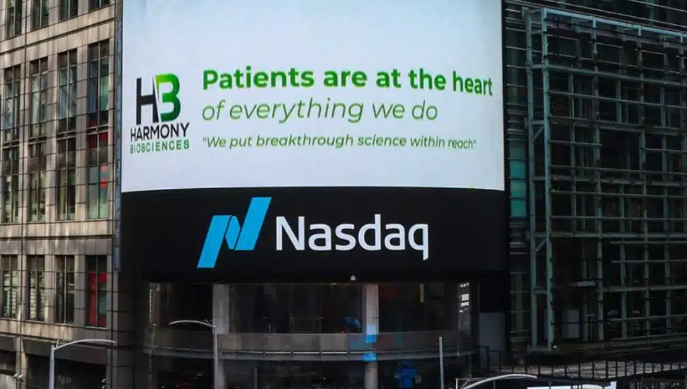 A sign for Harmony Biosciences stands above a sign for NASDAQ on a building in New York.