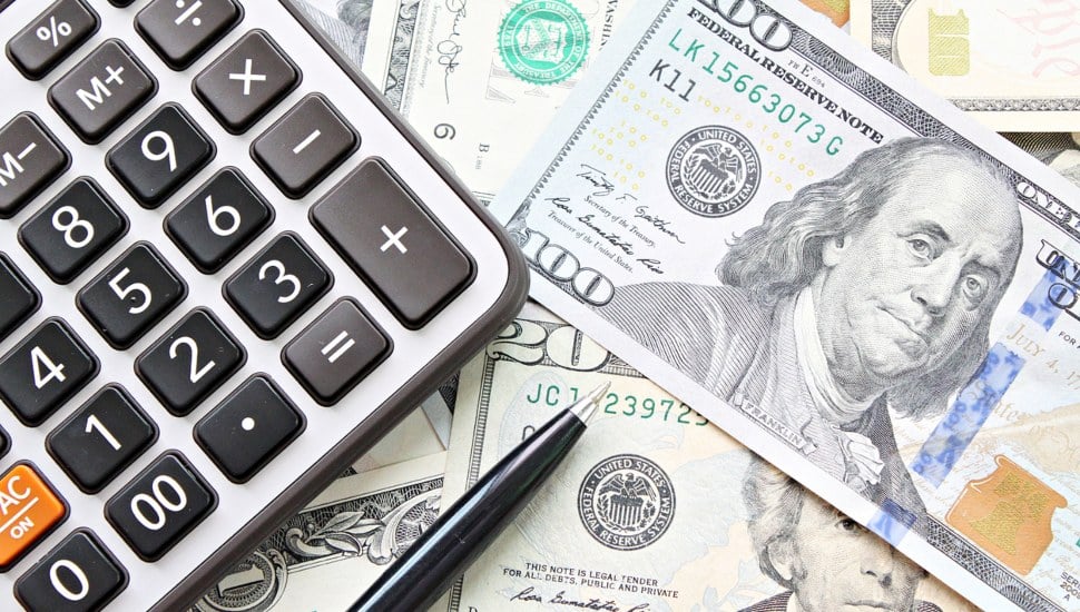 A pile of money with a calculator and a pen on top.
