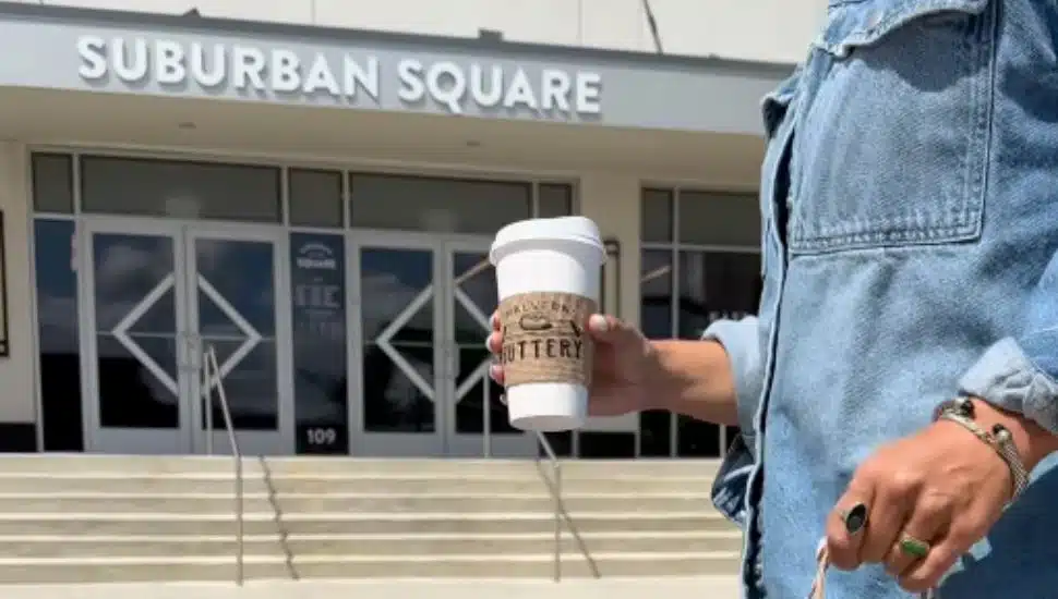 A woman carries a cup of coffee past Suburban Square in Ardmore.