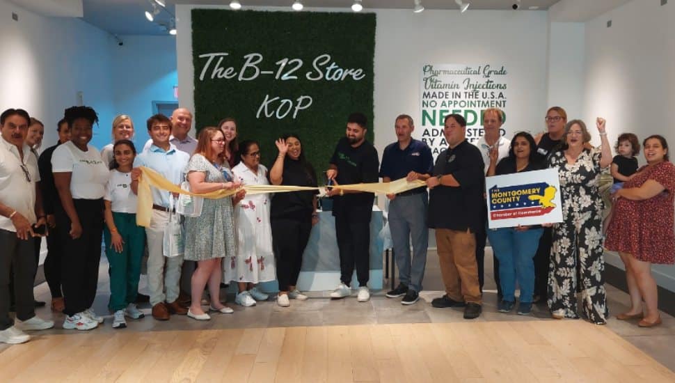 Group of people at the ribbon-cutting ceremony for The B-12 Store King of Prussia, including owner Arjun Patel, Montgomery County Chamber of Commerce representatives, and community members standing in front of the store’s green wall sign.