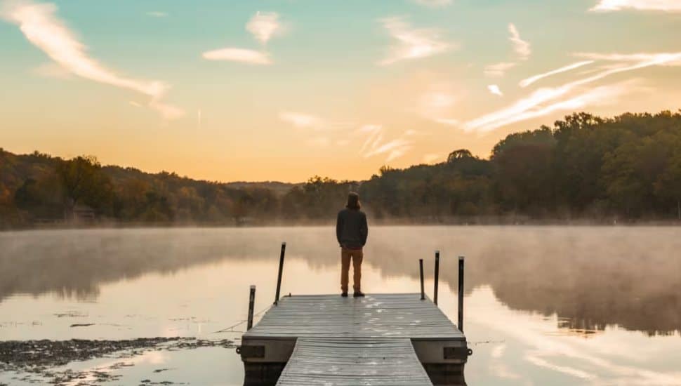 Person standing on a dock overlooking a misty lake at sunrise, surrounded by fall foliage in Montgomery County, PA.