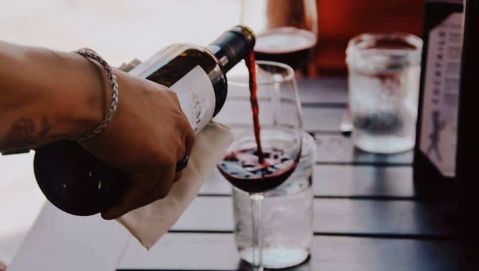 Hand pouring red wine into a glass at an outdoor restaurant table.
