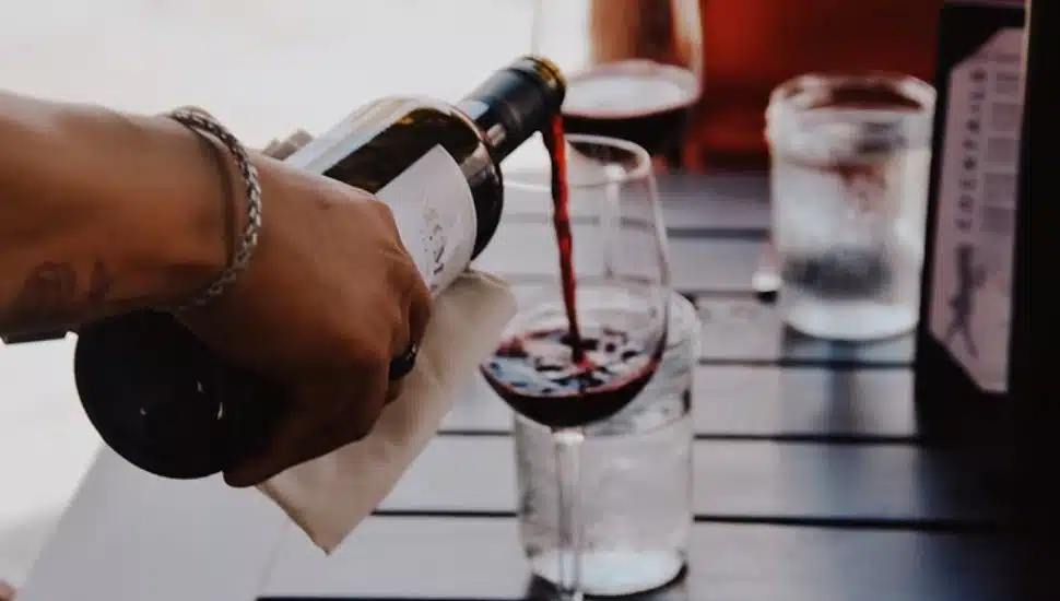 Hand pouring red wine into a glass at an outdoor restaurant table.