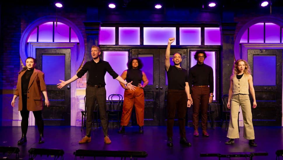 The Second City cast performs on stage under purple lights at Montgomery County Community College’s Montco Cultural Center.