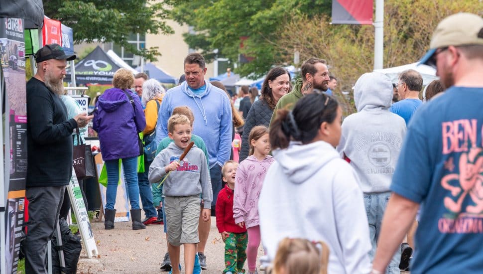 Families and children enjoy a lively afternoon at the Whitpain Community Festival with food vendors, games, and activities along a bustling walkway.