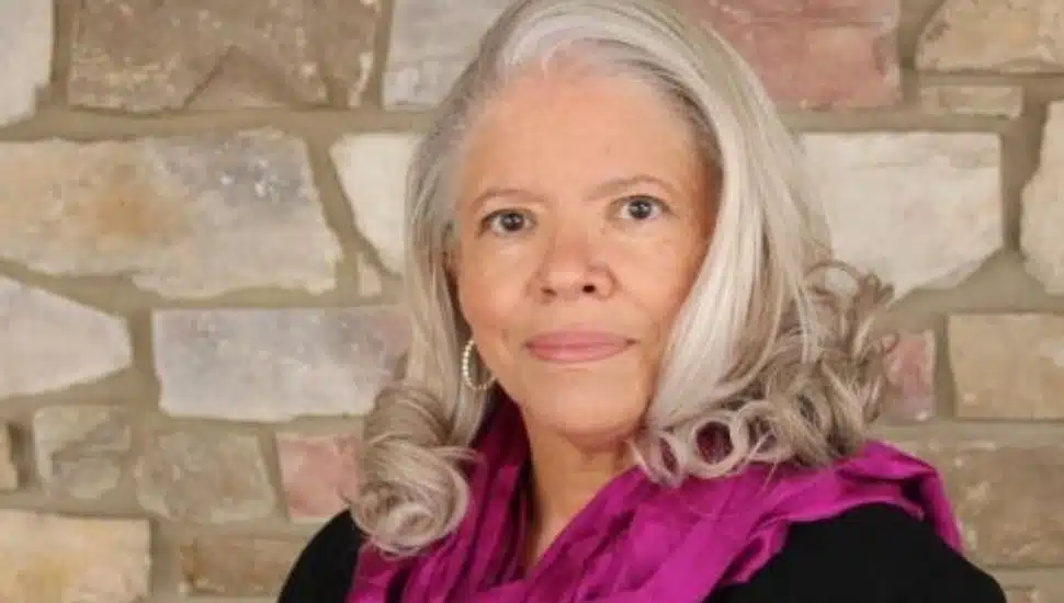Mayor Lillian DeBaptiste of West Chester, wearing a magenta scarf, poses in front of a stone wall for a professional portrait.