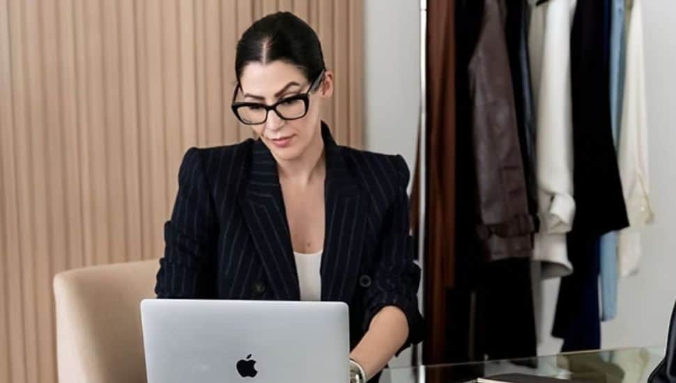 Amanda Wood upper body headshot as she types on Apple laptop with clothing rack in background.