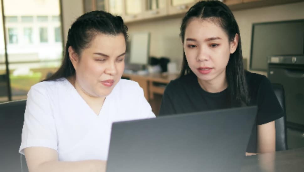 Two women take a virtual training course on a laptop.