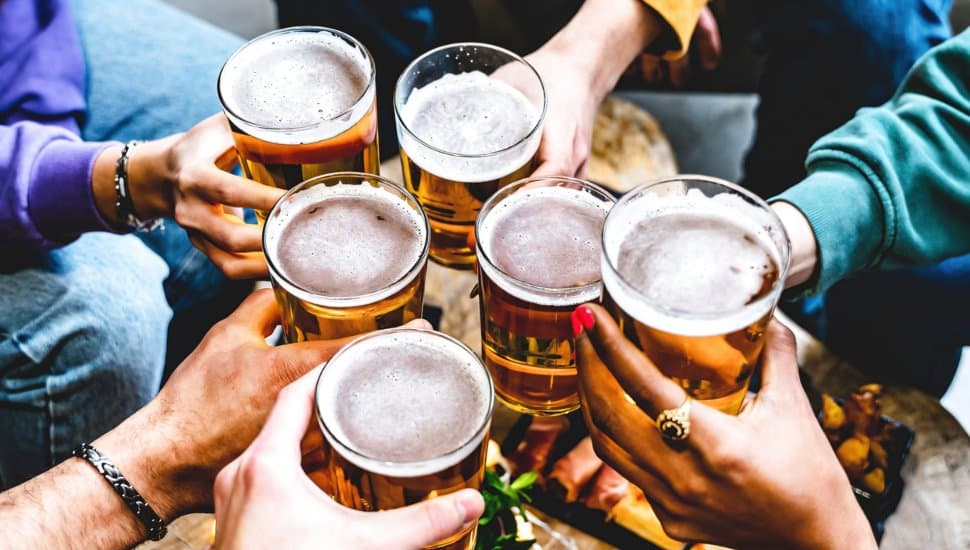 A group of young people cheering glass of beer together at brewery.