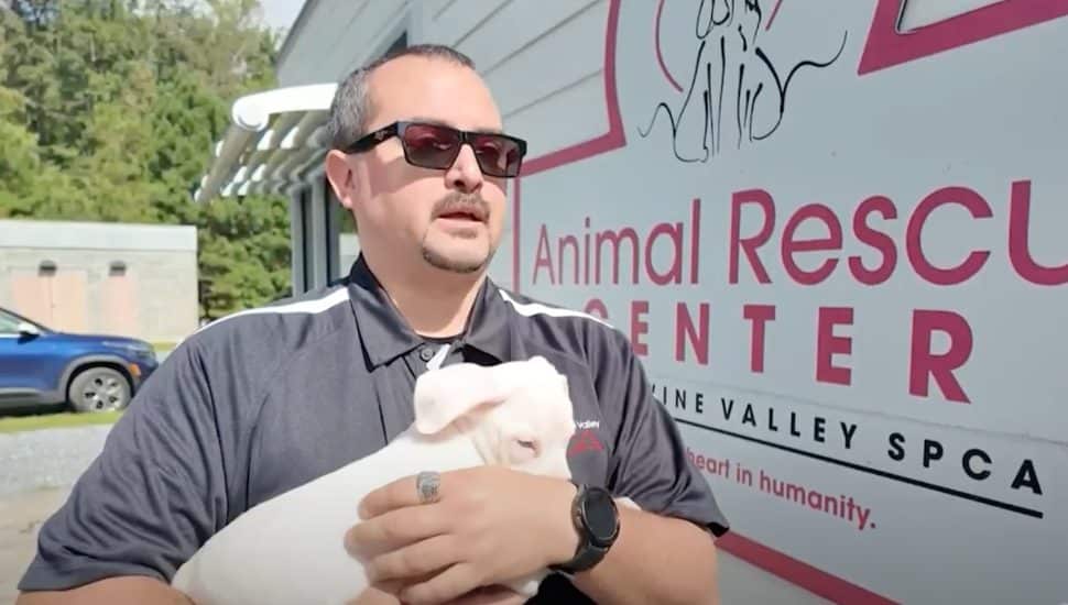 A Brandywine Valley SPCA team member holding a small dog in front of an SPCA vehicle.
