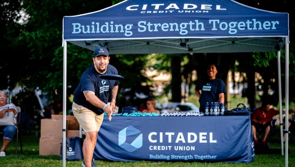 Credit union employee throws a frisbee outdoors.