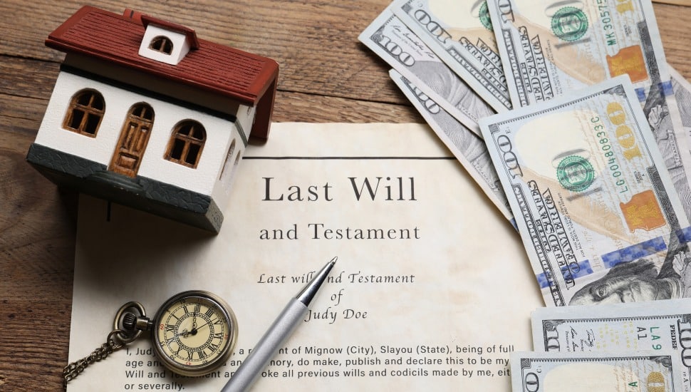 Last Will and Testament, pocket watch, dollar bills, house model and pen on a wooden table.