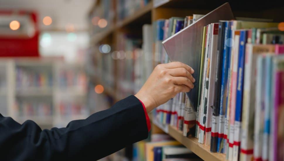 Hand reaches for book on library shelf.