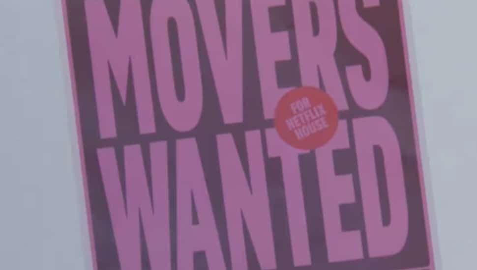 A Movers Wanted poster for Netflix House hangs on a wall.