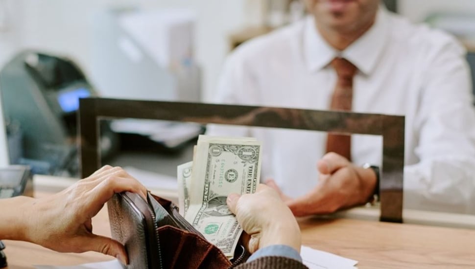 Person takes money out of wallet to give to bank teller.