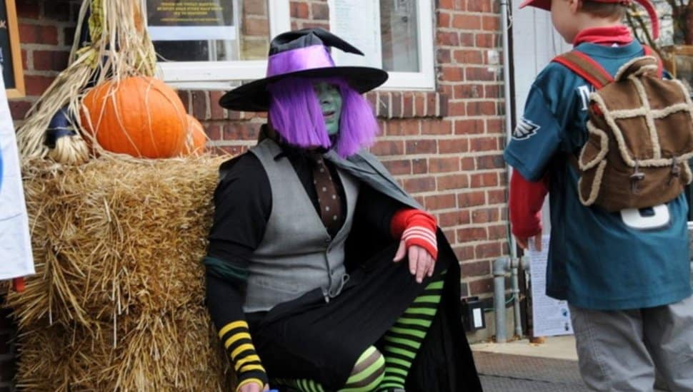 A costumed witch with green face paint and a purple wig greets a child during the Witches of Narberth Halloween event in Montgomery County.