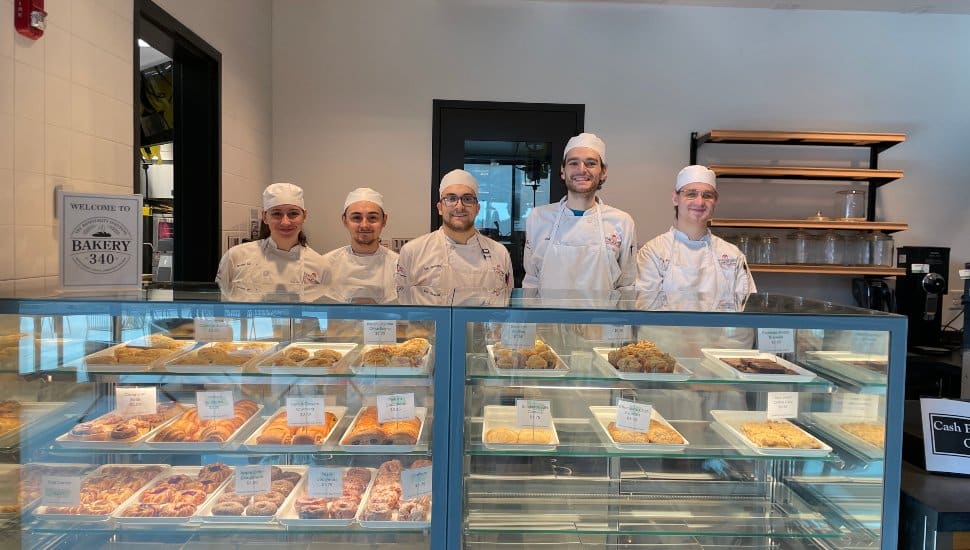 Montgomery County Community College culinary arts students in chef uniforms standing behind a bakery display case filled with pastries at Bakery 340.