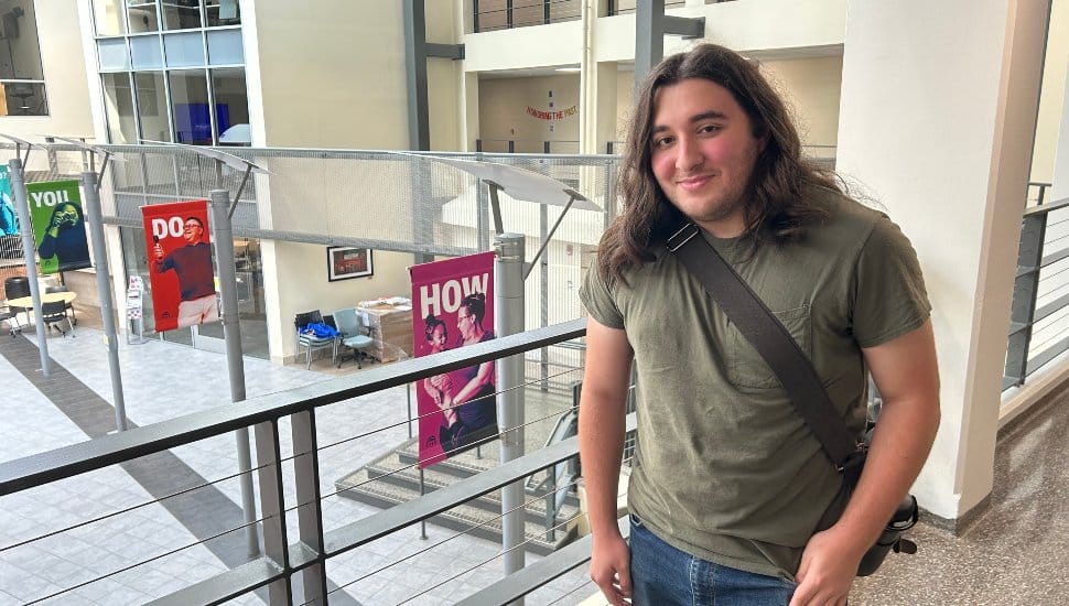 History major Juan Aguilar stands in a green T-shirt at MCCC, smiling.