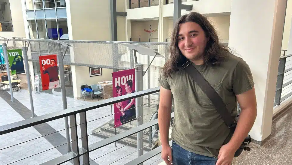 History major Juan Aguilar stands in a green T-shirt at MCCC, smiling.