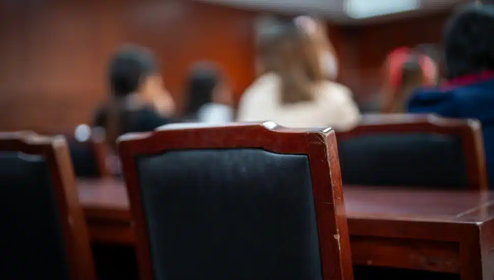 A group of people are sitting in a room with wooden chairs. The chairs are black and the room is dimly lit
