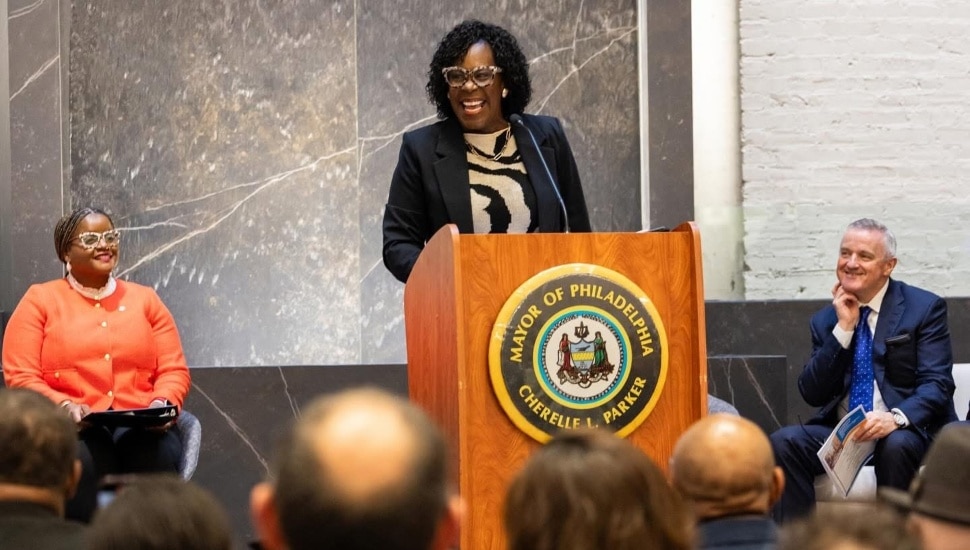 Cherelle Parker smiling while at the podium with people behind her and a crowd in front of her.