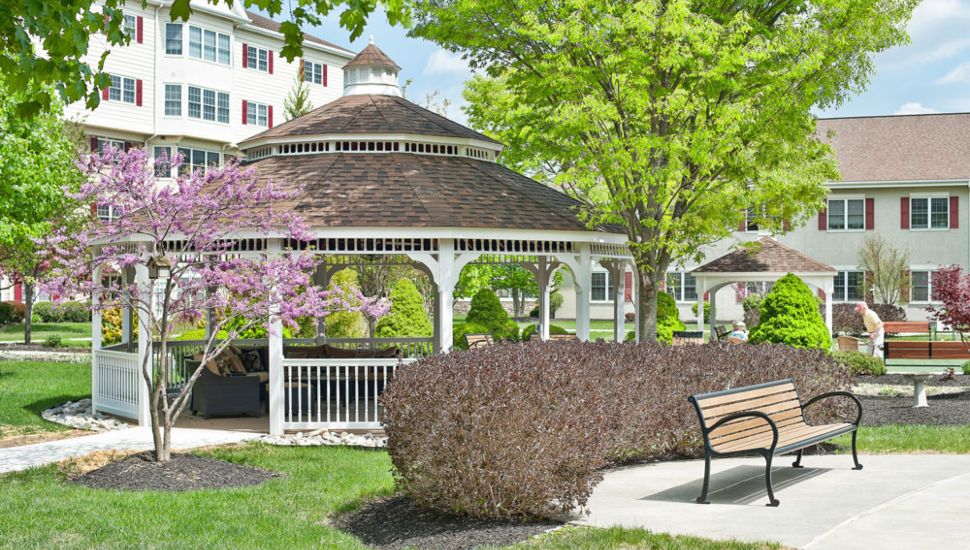 A gazebo, trees, park benches, bushes and a pathway outside Freedom Village at Brandywine retirement community.