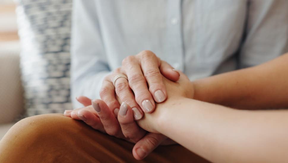 Two grieving people hold hands.