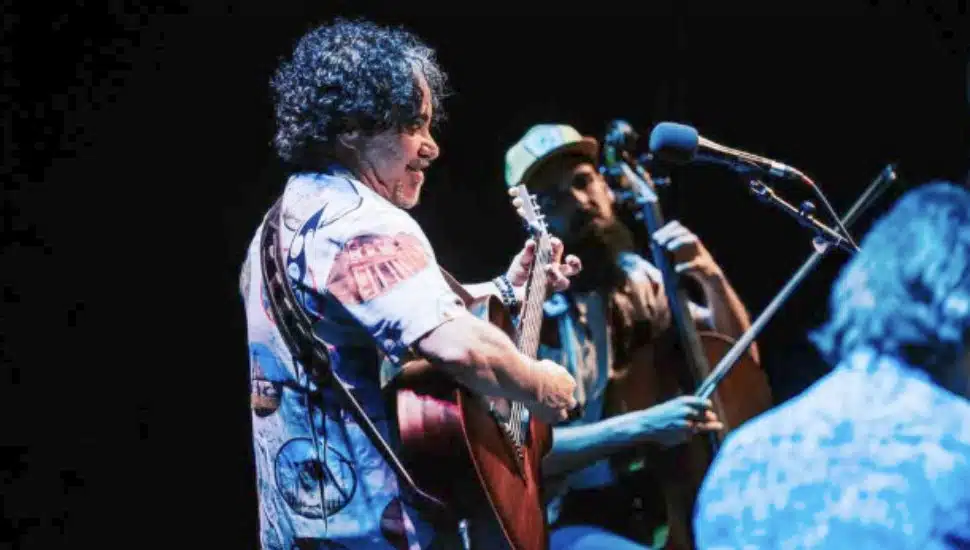 John Oates strums his guitar onstage with his band.