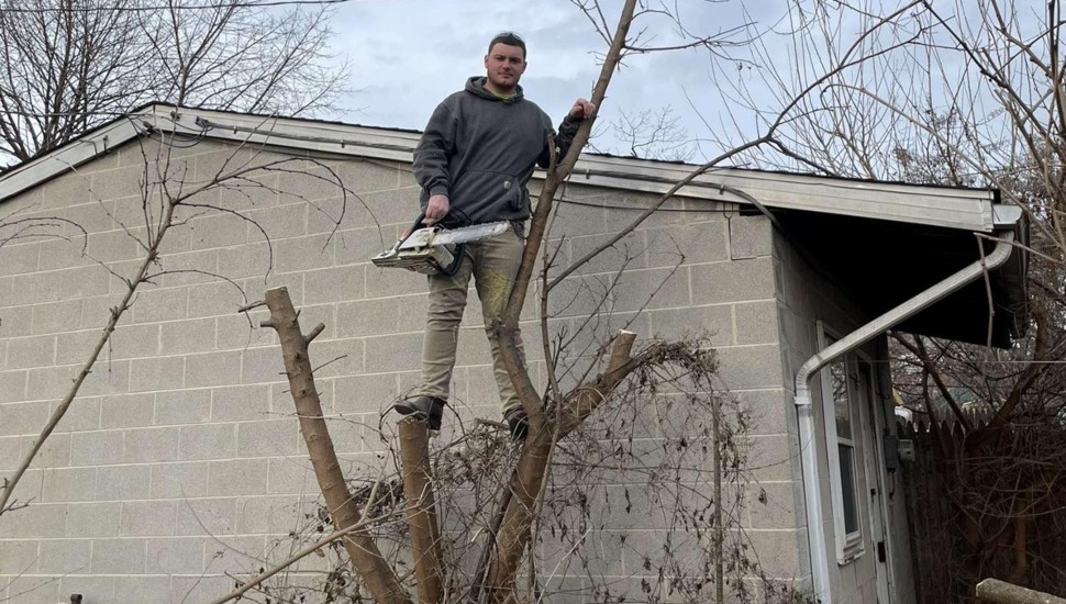Man stands on tree stump with chainsaw.