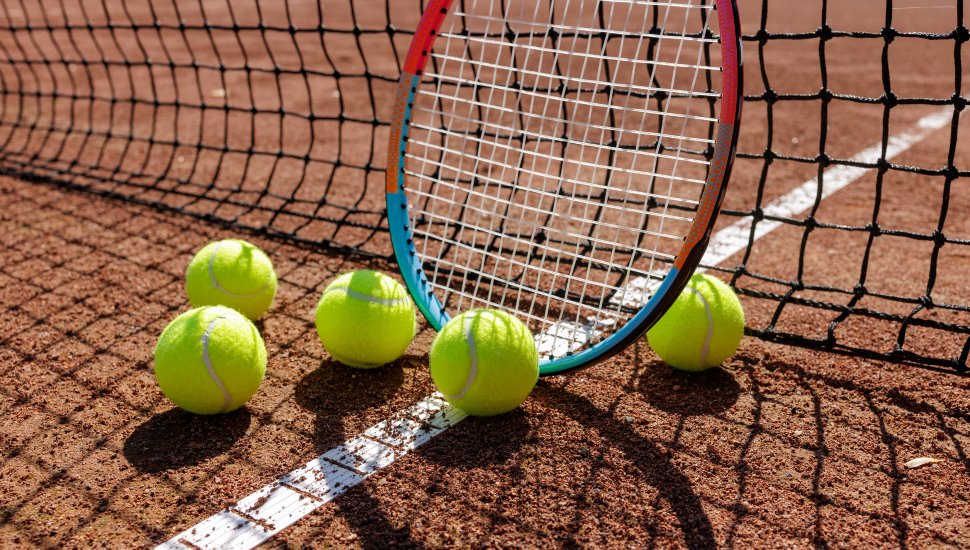 Closeup racket and bright balls on clay line under a net shadow.
