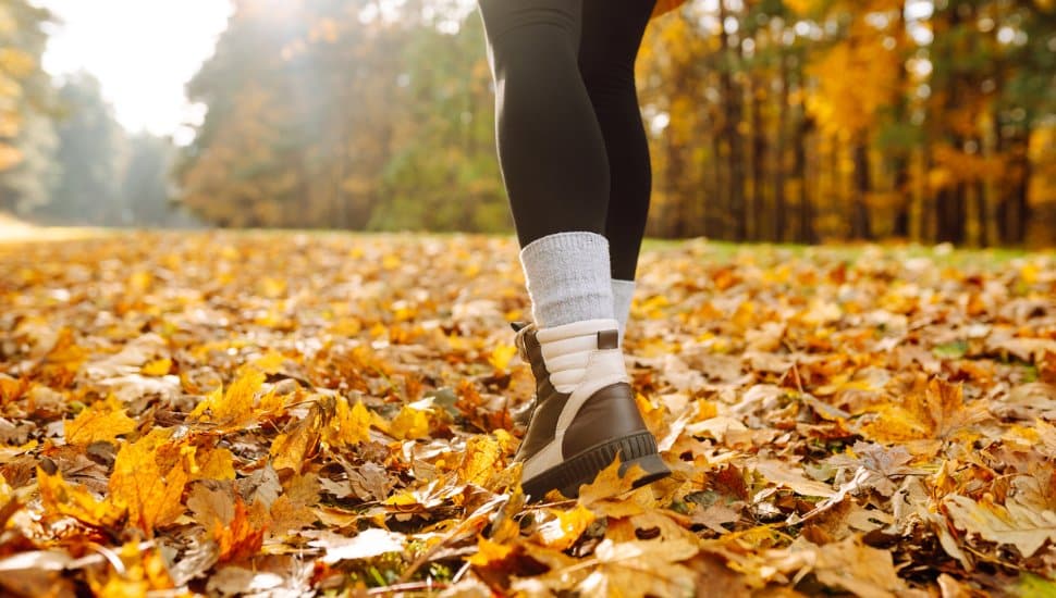 A woman walks through leaves on a trail.