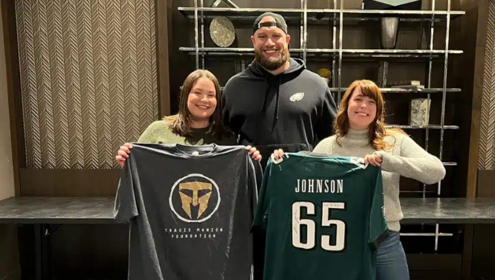 Philadelphia Eagles offensive lineman Lane Johnson with two women holding a Lane Johnson jersey and a sweatshirt for the Travis Manion Foundation.