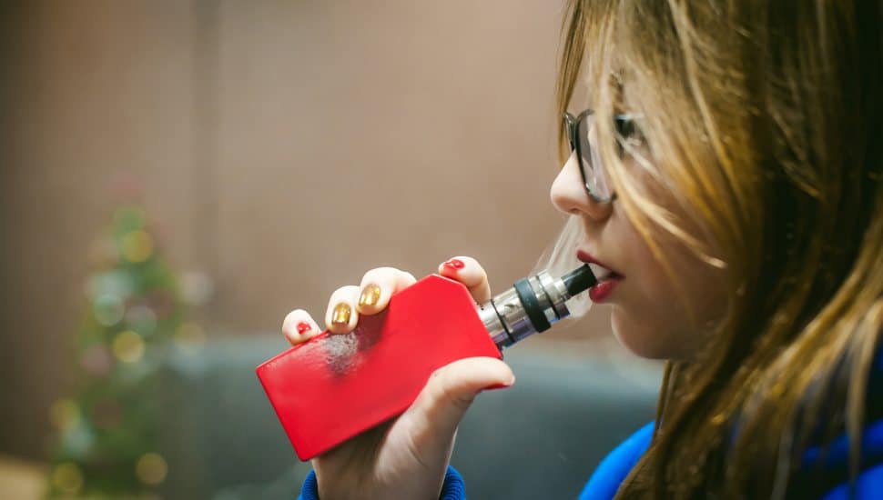 A teen inhales from a nicotine vape.