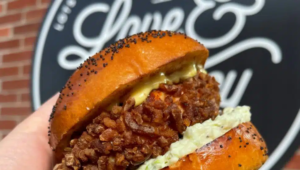 A fried chicken sandwich is held outside of a Love & Honey Fried Chicken restaurant.