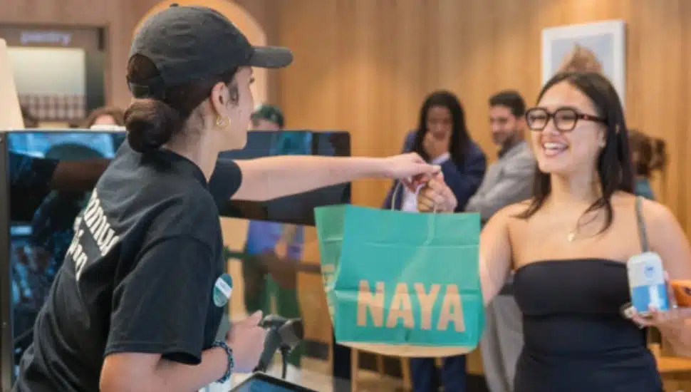 A Naya associate hands a customer a branded bag over the counter.