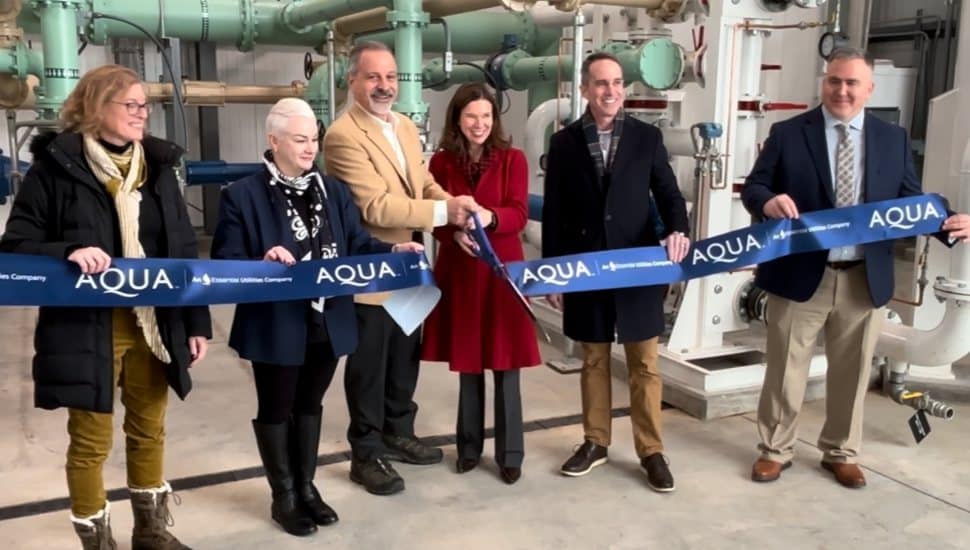 Group of officials holding an AQUA ribbon during a ribbon-cutting ceremony inside a utility facility.