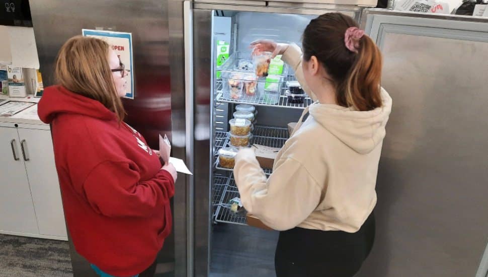 Students pull prepared food from an industrial refrigerator.
