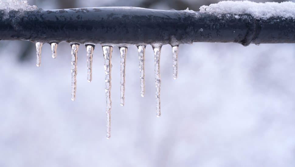 Frozen icicles on a gray pipe after a thaw in winter.