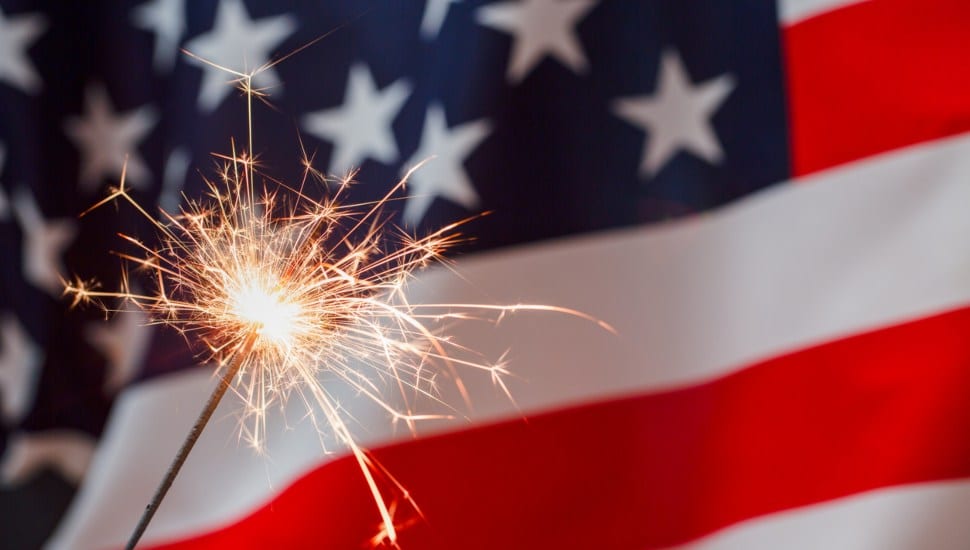 A sparkler flashes in front of an American flag.