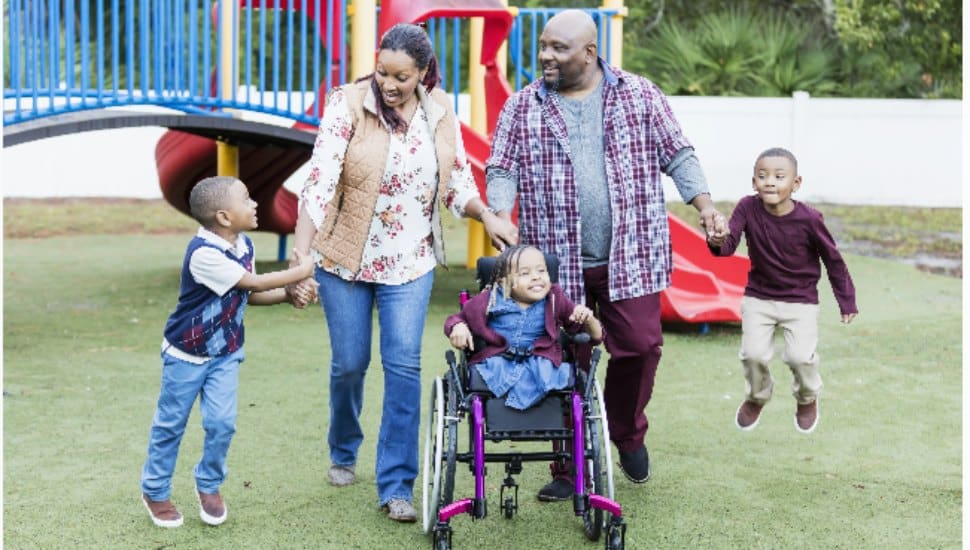 A happy family with a child in a wheelchair at a playground.