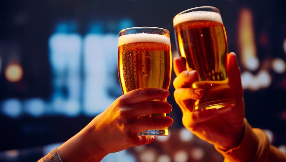 Hands holding lager light foamy big beer glasses and clinking.