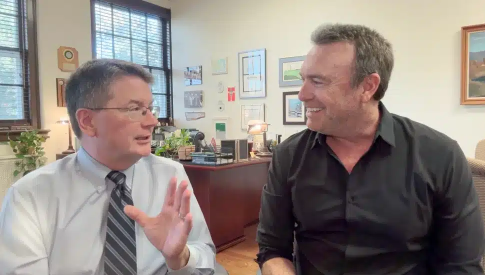 Two men speak in front of a camera.