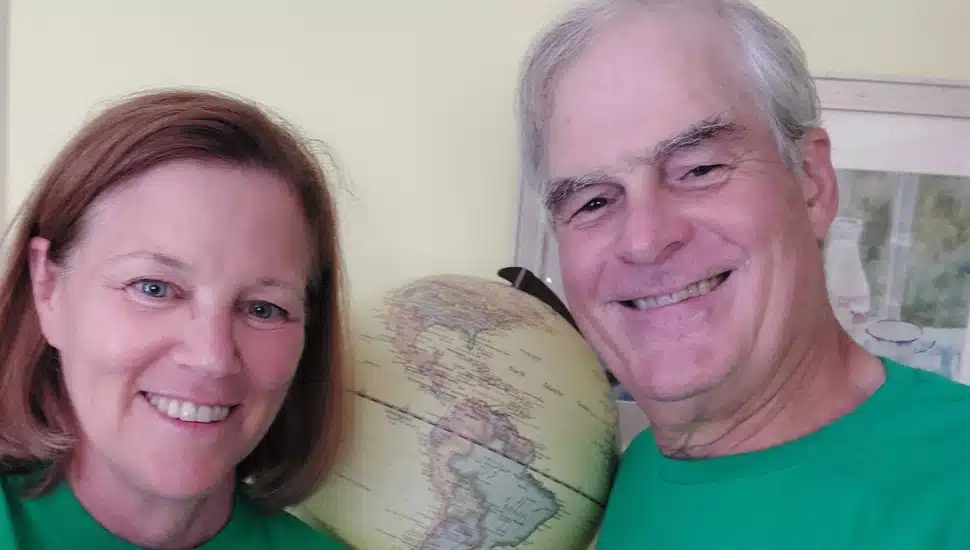 Retired man and woman smile next to a globe.