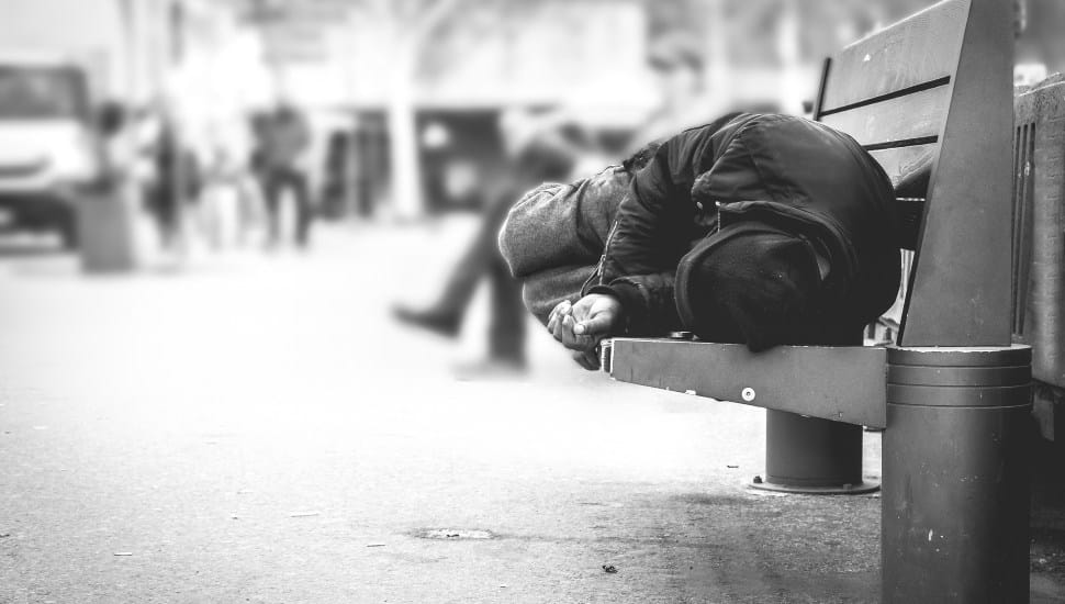A homeless man sleeps on a public bench.
