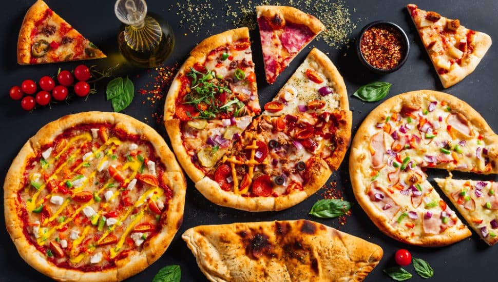 An assortment of pizza pies lay surrounded by ingredients.
