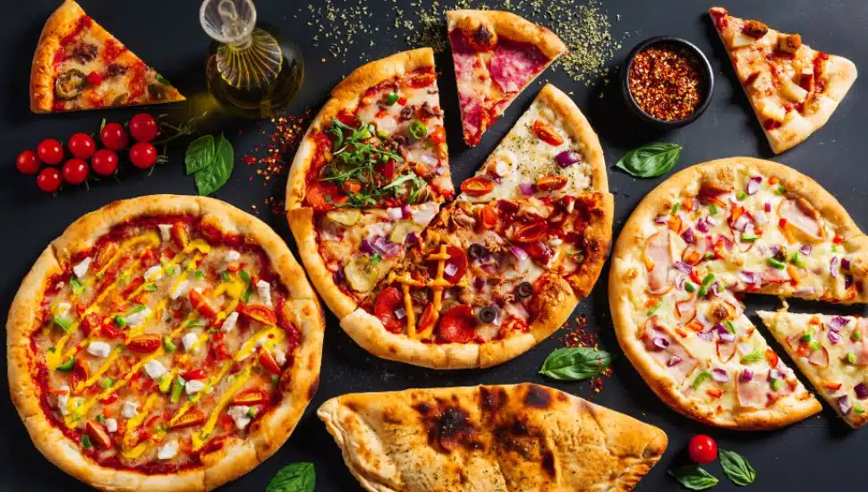 An assortment of pizza pies lay surrounded by ingredients.