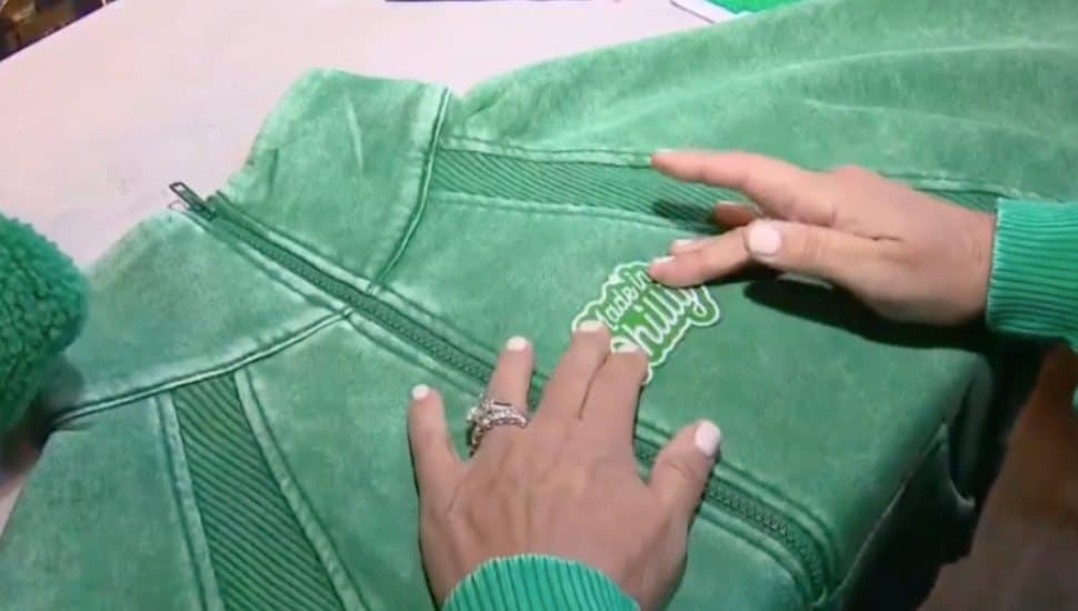 Primitive Boutique owner Ann Martinelli places a 'Made in Philly' patch on a green sweater.