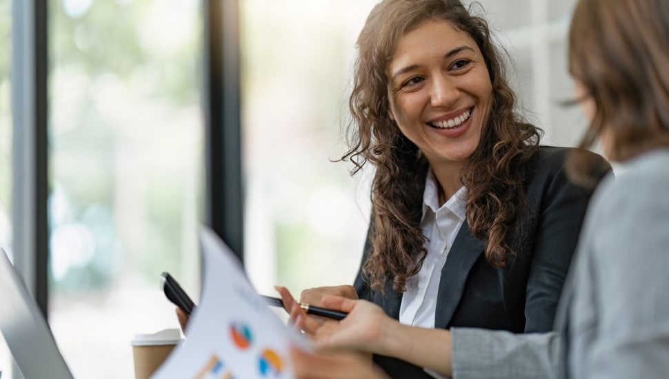 Businesswomen discuss financial report paperwork in office.