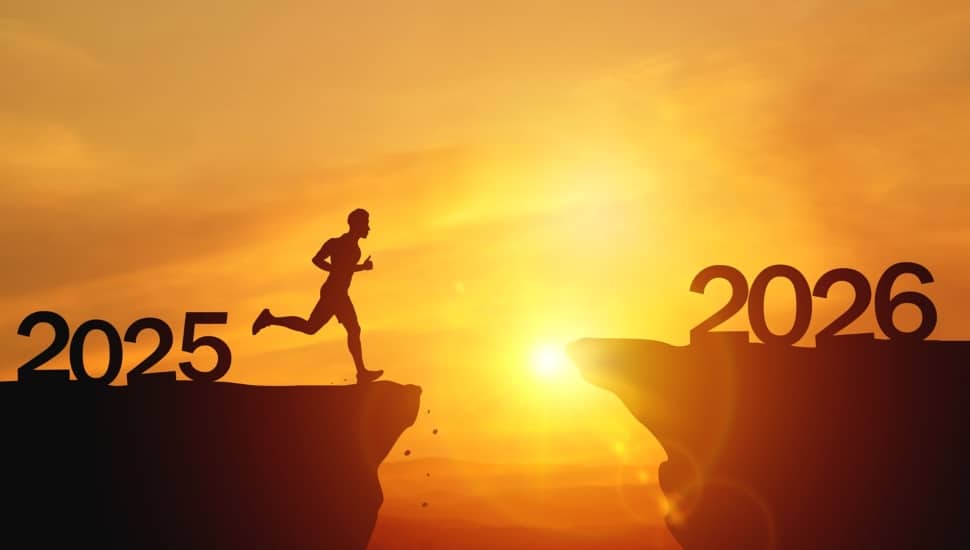 Silhouettes of human jumping over cliff toward finish line on sunset.